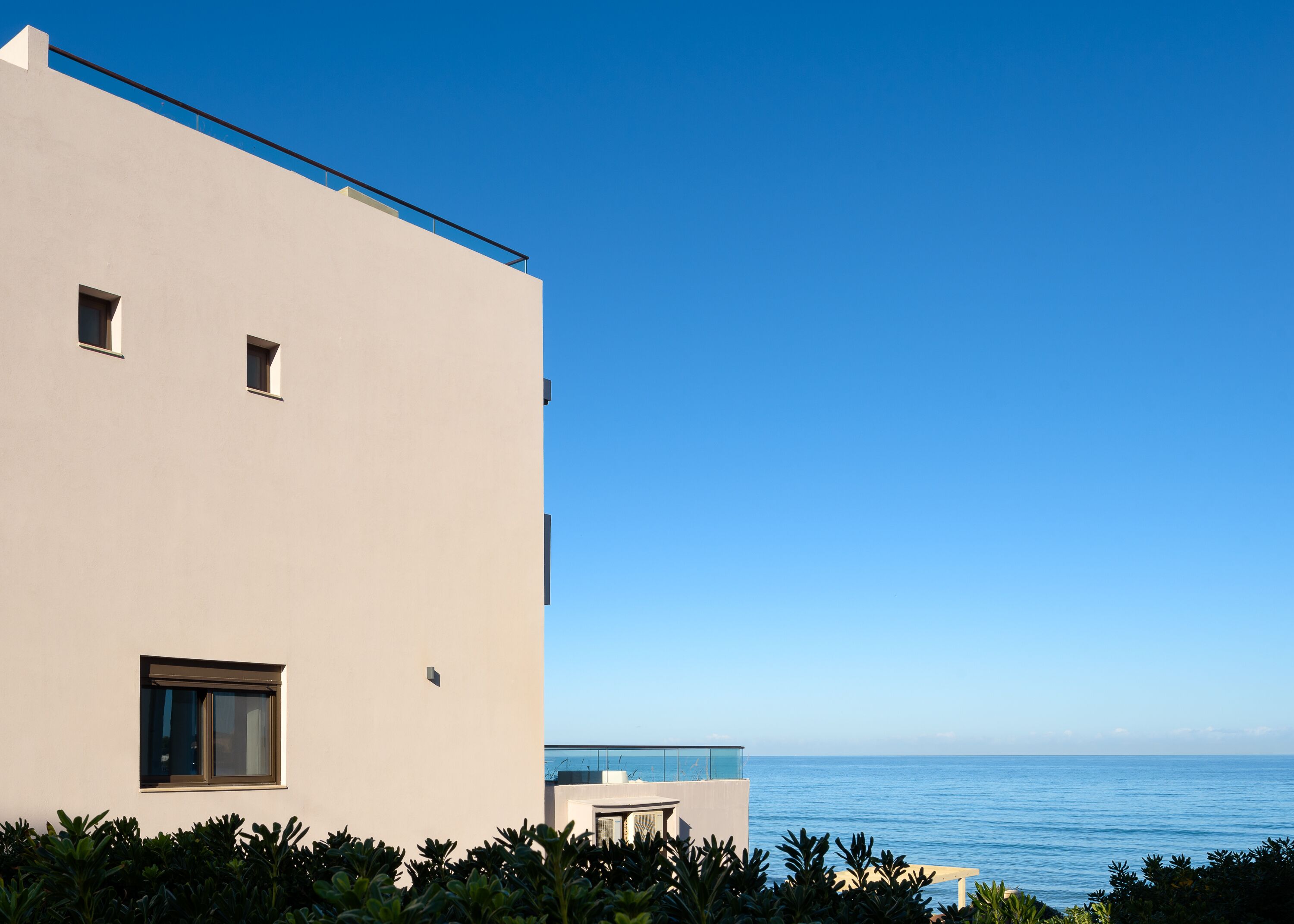 Ein modernes Gebäude mit flacher Fassade, einem kleinen Fenster und einem Balkon mit Meerblick.