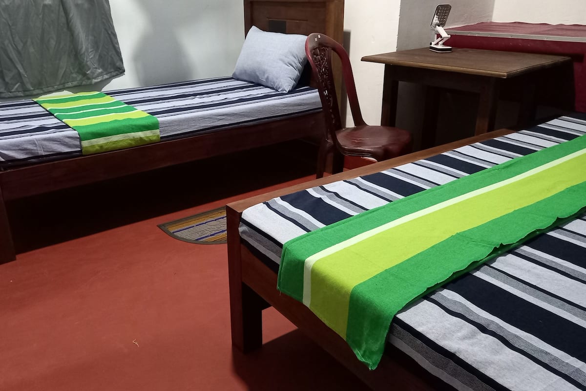 Deux lits simples avec du linge de lit à rayures, une chaise en bois, une petite table et un sol recouvert d’une moquette rouge.