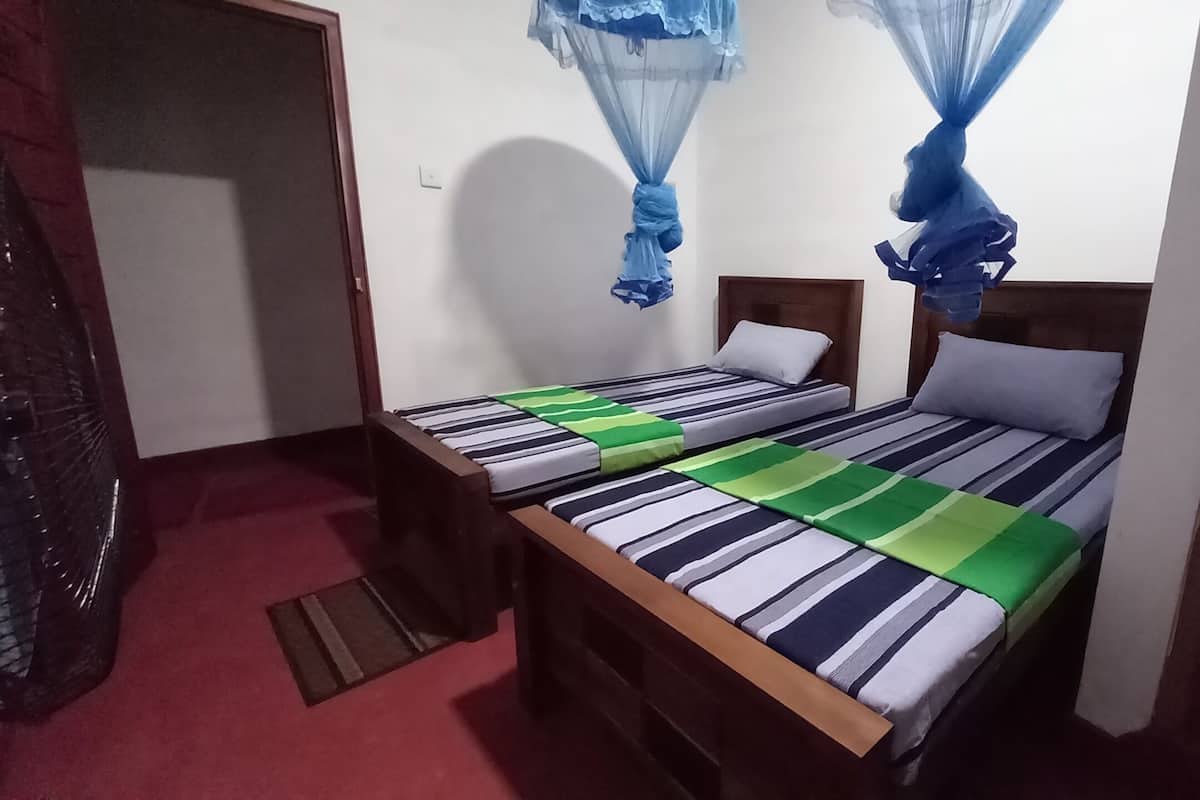 Une petite chambre avec un lit simple, une couvre-lit à rayures, une tête de lit en bois et une moustiquaire au-dessus du lit.