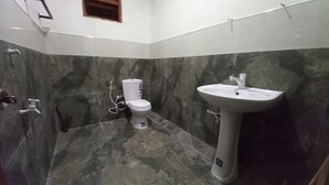 A bathroom with a toilet and a pedestal sink, both in white, against a grey and black marble wall. - Sewana Guest INN (Wellawaya)