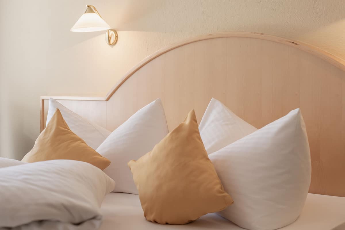 A neatly made bed with white and beige pillows, a wooden headboard, and a wall-mounted lamp.