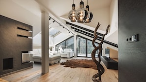 Una sala de estar moderna con techo alto, piso de madera, un ventanal grande y una lámpara escultórica original.