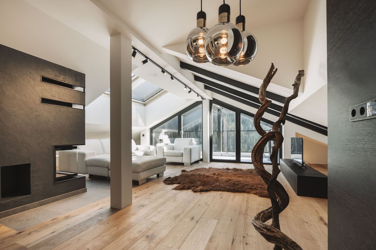 A modern living room with a high ceiling, wooden flooring, a large window, and a unique sculptural light fixture.