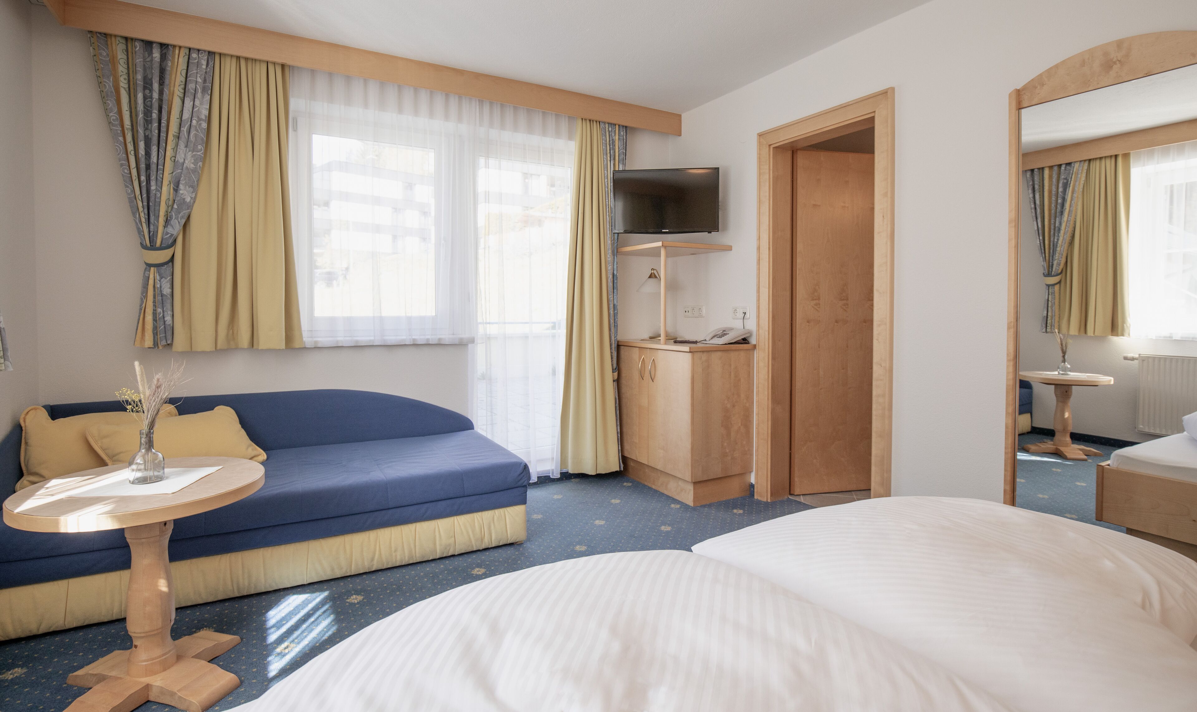 Ein Hotelzimmer mit Bett, Sofa, Schreibtisch mit Stuhl, Fernseher und Spiegel.