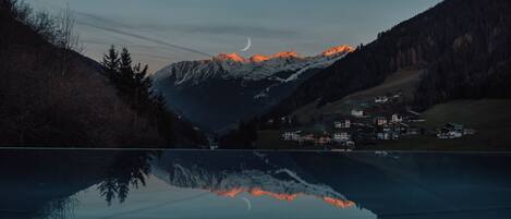 A mountain landscape with a lake reflecting the scenery, including snow-capped peaks and a crescent moon.