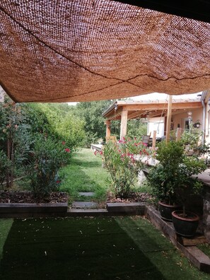 Uma área de varanda coberta com pérgola, gramado e plantas em vasos.