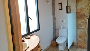 Un baño con tocador de madera, inodoro y zona de ducha.