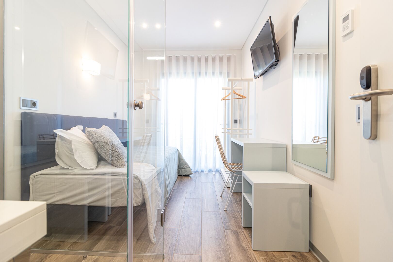 Une chambre d’hôtel moderne équipée d’un lit, d’un bureau, d’une chaise, d’une télévision et d’un miroir.