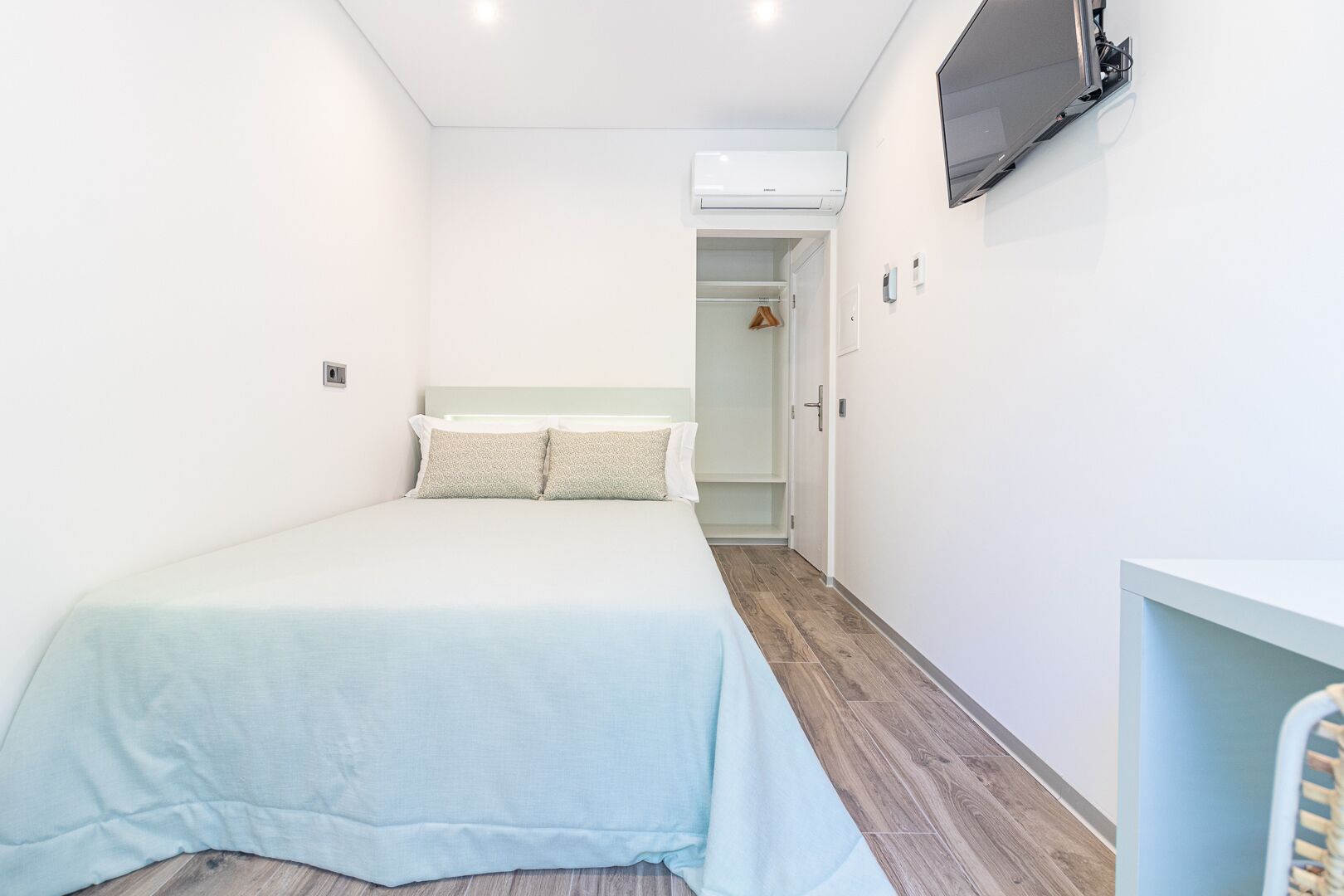 A bedroom with a bed, a TV mounted on the wall, and a wardrobe.