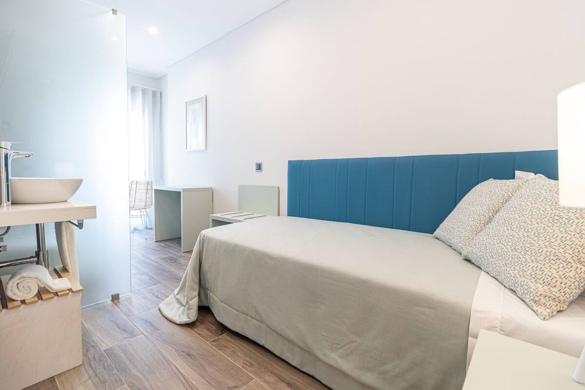 A modern hotel room with a bed, a bedside table, a sink, and a chair.