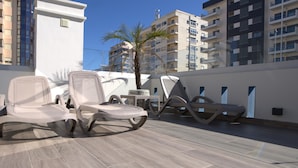Terraza en la azotea con sillones modernos, una mesa pequeña y una palmera.