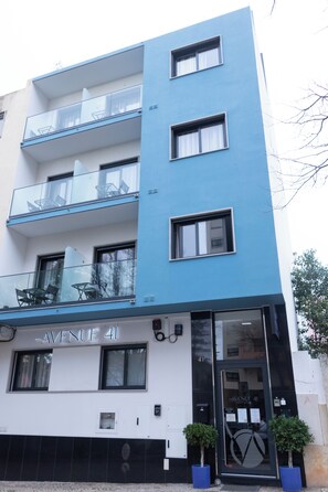 A modern building with a sign reading "AVENUE 41". It features multiple balconies with glass railings and potted plants at the entrance. - Avenue 41 Guest House (Faro)