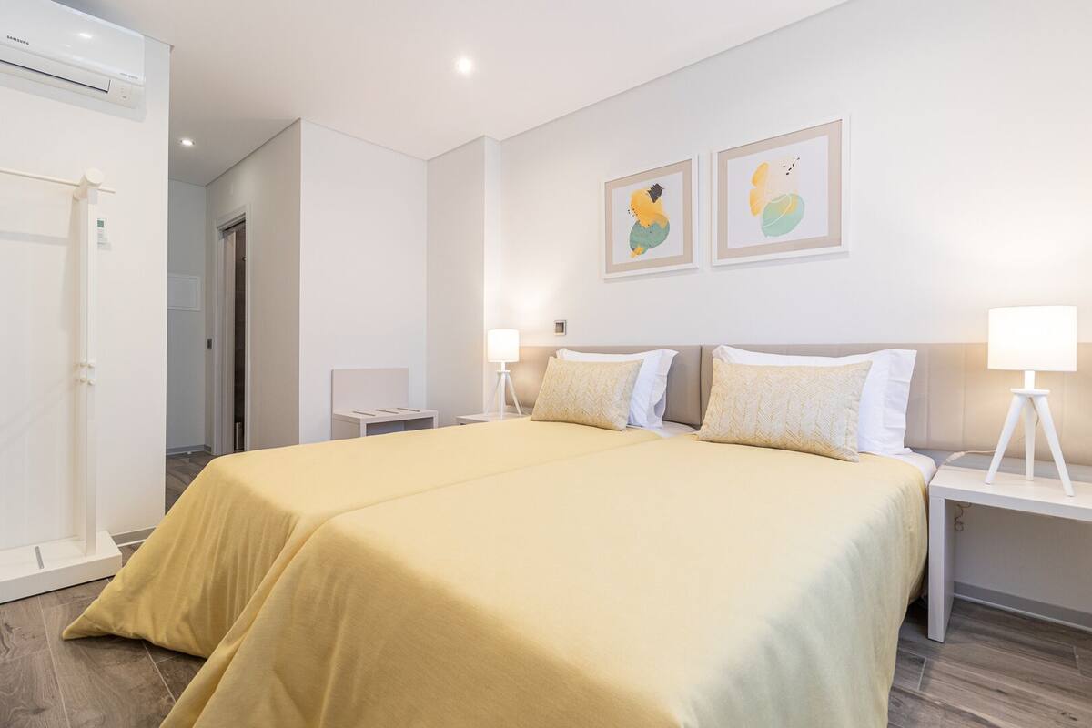 A hotel room with a large bed, two bedside tables with lamps, a wardrobe, and two framed artworks on the wall.