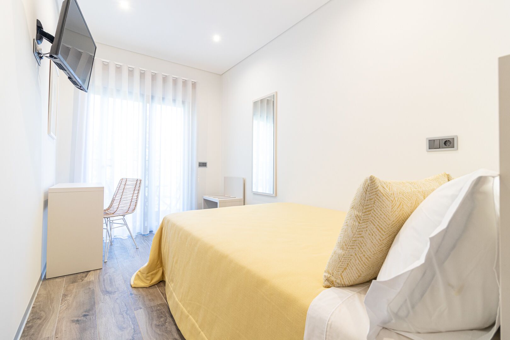 A hotel room with a bed, a desk, a chair, and a TV mounted on the wall.