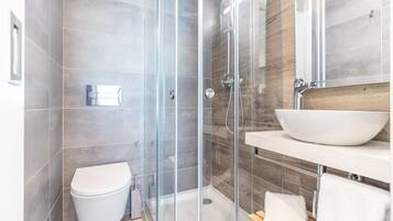 A modern bathroom with a glass-enclosed shower, a white toilet, and a wooden vanity with a large white basin.