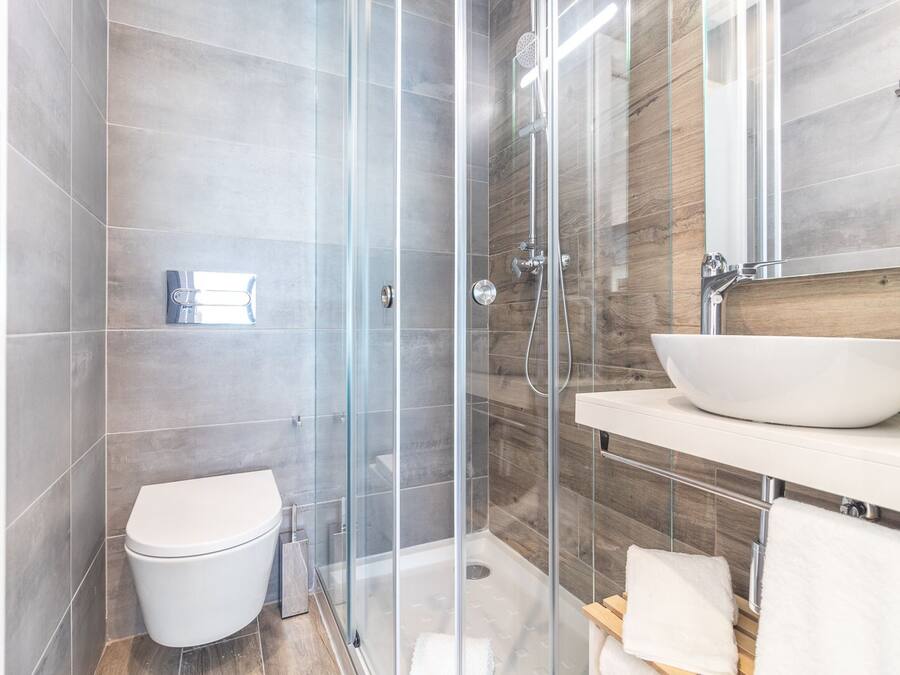 A modern bathroom with a glass-enclosed shower, a white toilet, and a wooden vanity with a large white basin.