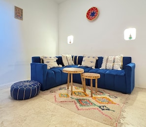 A blue sofa with patterned cushions, two small wooden tables, a blue ottoman, and a colorful rug. - Dar Kamilya. Maison au Centre de la Medina (Marrakech)