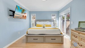 A bedroom with a bed, a TV mounted on the wall, a dresser, and a window with an 'EXIT' sign. - Beach Paradise : Family-Friendly + Free Parking (Hollywood)