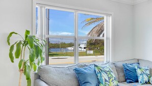 A room with a grey sofa, a potted plant, and a large window with a view of the sea and a boat. - Beach Paradise : Family-Friendly + Free Parking (Hollywood)