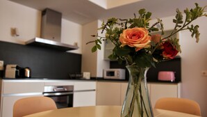 A modern kitchen with white cabinets, a black countertop, and a vase with flowers on a round table. - TERCERO A - 3 A -APARTAMENTOS ALMADA - Plaza del Pilar (Zaragoza)