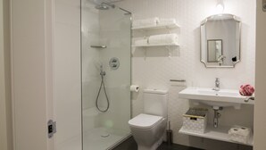 A modern bathroom with a glass-enclosed shower, a white toilet, a sink with a mirror, and shelves with towels. - TERCERO A - 3 A -APARTAMENTOS ALMADA - Plaza del Pilar (Zaragoza)
