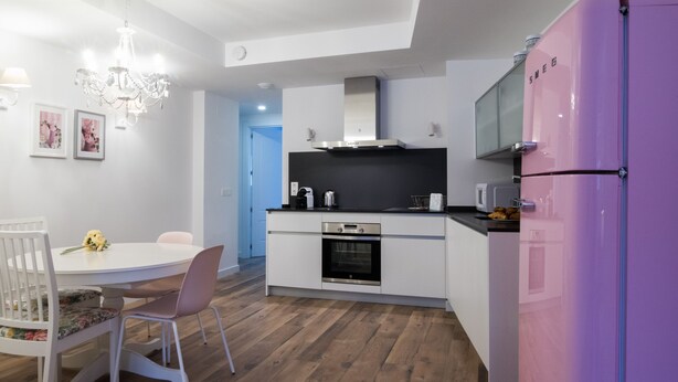 A modern kitchen with white cabinetry, a pink refrigerator, a dining table with chairs, and a chandelier. - TERCERO A - 3 A -APARTAMENTOS ALMADA - Plaza del Pilar (Zaragoza)