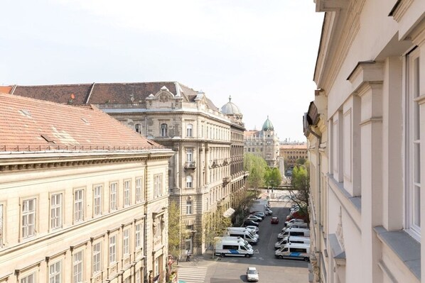 A street view with historic buildings, parked cars, and a clear sky.