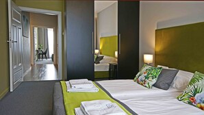 A hotel room with two beds, a green bed runner, and a view of a hallway with a dining area. - IRS ROYAL APARTMENTS - IRS Brabank (Gdansk)