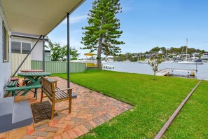 A patio with picnic tables and a bench, overlooking a marina with boats.