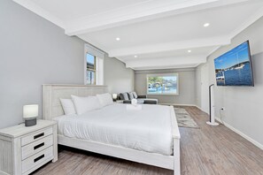 Un dormitorio con cama, mesita de noche, lámpara y televisor en la pared.