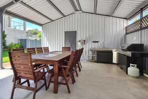 A covered outdoor kitchen area with a dining table and chairs, a grill, and a water heater.