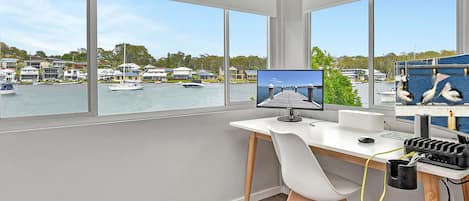 Ein moderner Arbeitsraum mit Schreibtisch, Stuhl und Computermonitor, mit Blick auf eine Marina mit Booten und Häusern.