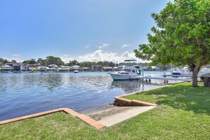 Un puerto deportivo con barcos amarrados, un área con césped y un árbol, y casas al fondo.