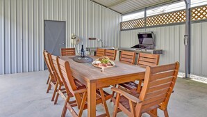 Un espacio de comedor al aire libre cubierto, con una mesa dispuesta para seis personas, rodeada de sillas de madera.