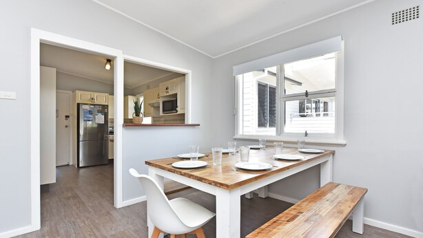 Una cocina moderna con armarios blancos, un refrigerador de acero inoxidable y una mesa de comedor de madera para seis personas.