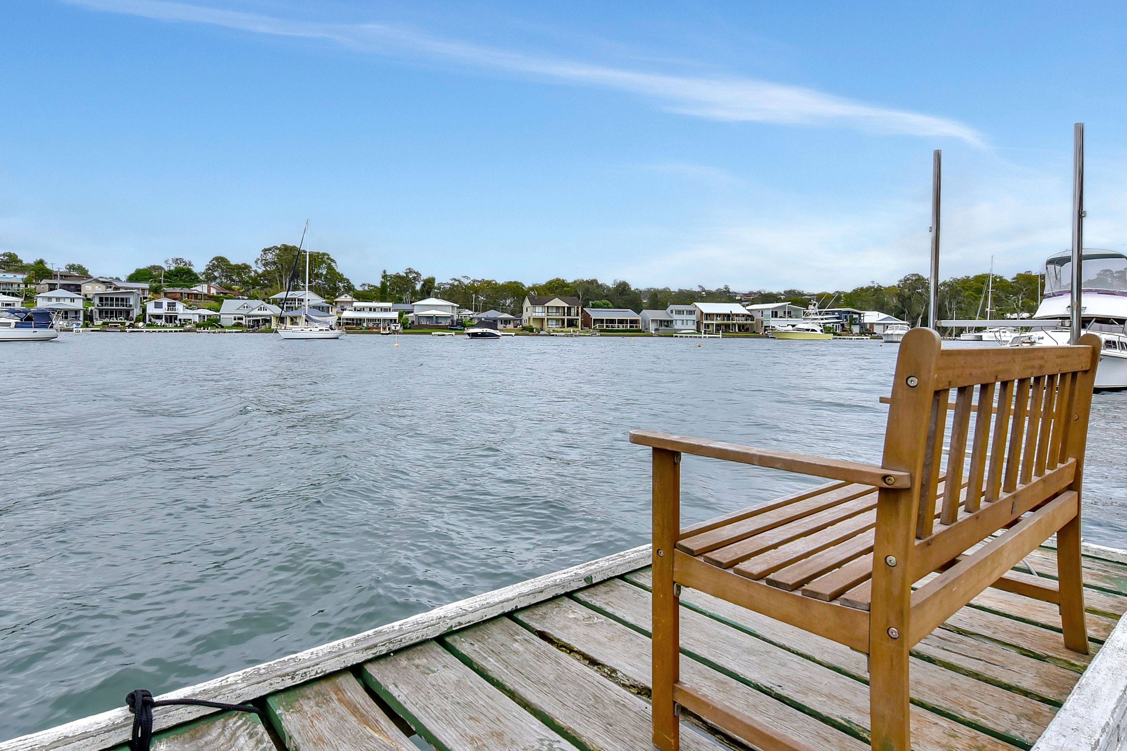 A wooden bench on a dock overlooking a marina with boats and houses in the background.