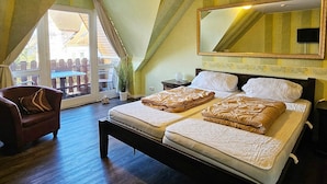 Une chambre avec un grand lit, une chaise, un miroir et une vue sur l’extérieur, visible à travers une porte vitrée.