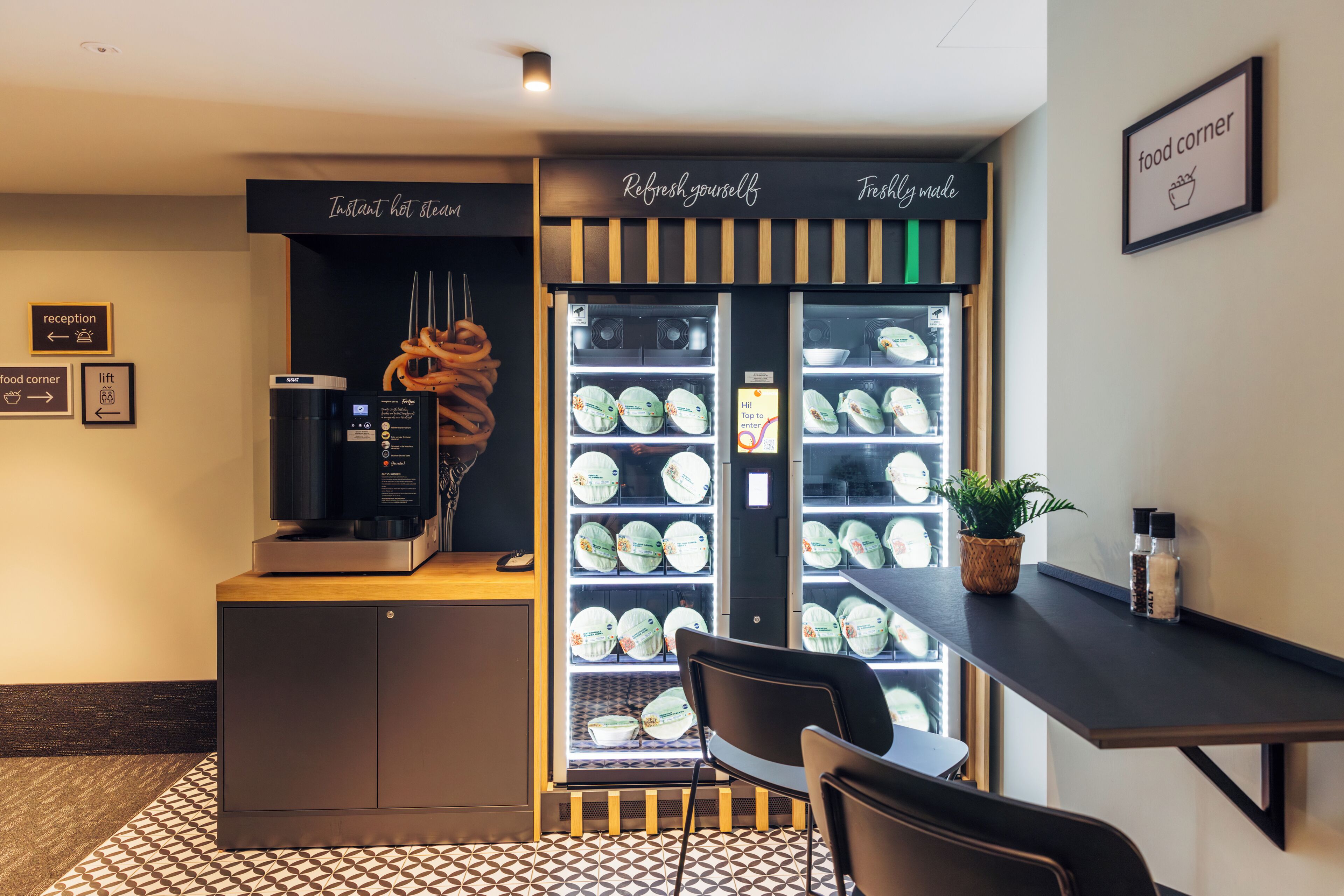 Un comptoir où l’on sert des plats, avec une machine à café, un espace avec des chaises et un présentoir d’assiettes.