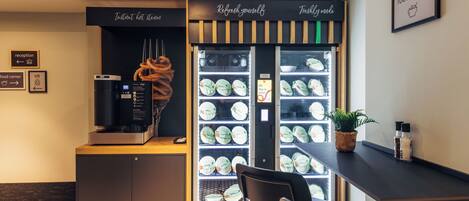 Un comptoir où l’on sert des plats, avec une machine à café, un espace avec des chaises et un présentoir d’assiettes.