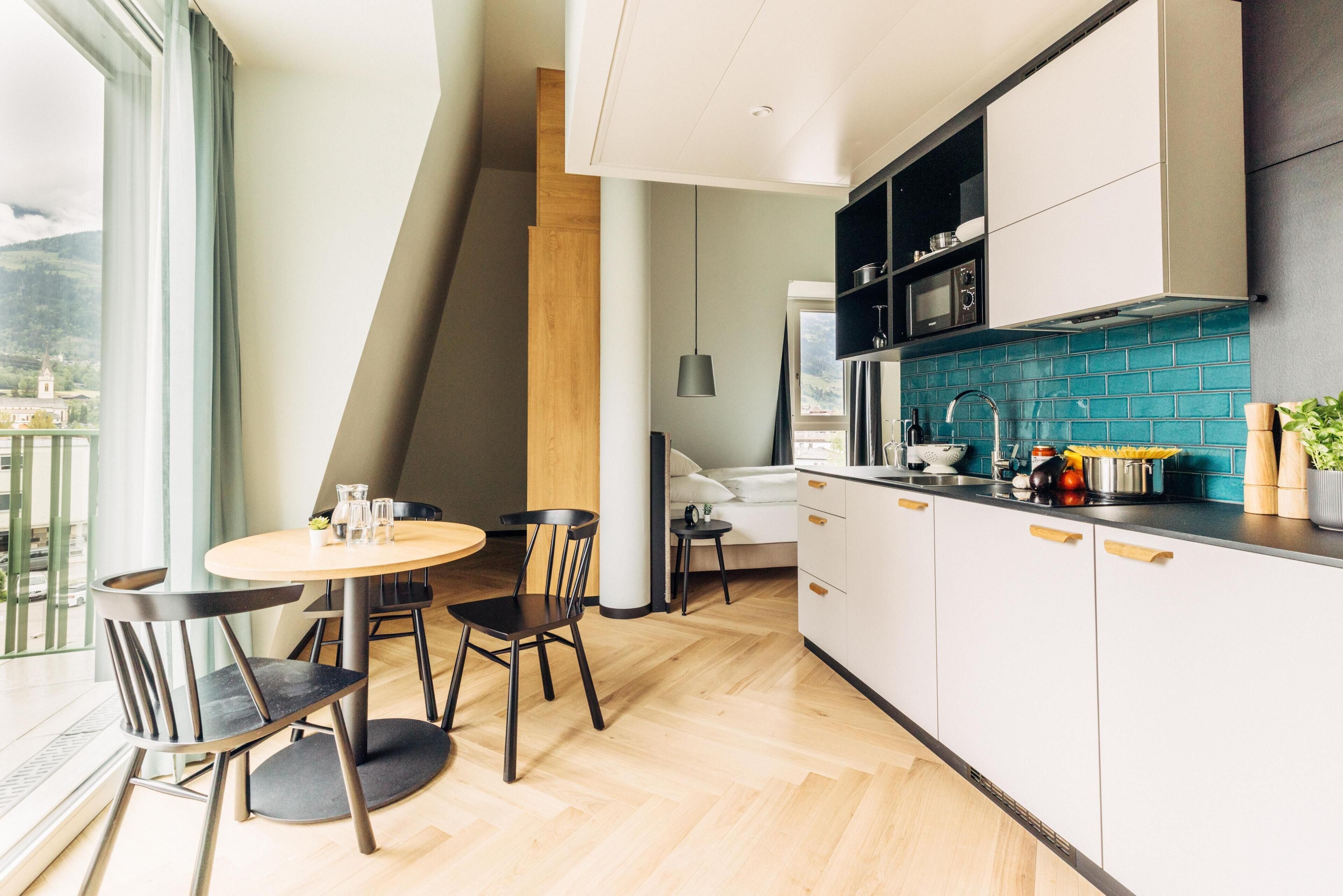 Una cocina moderna con gabinetes blancos, un salpicadero azul y un comedor con una mesa redonda y sillas.