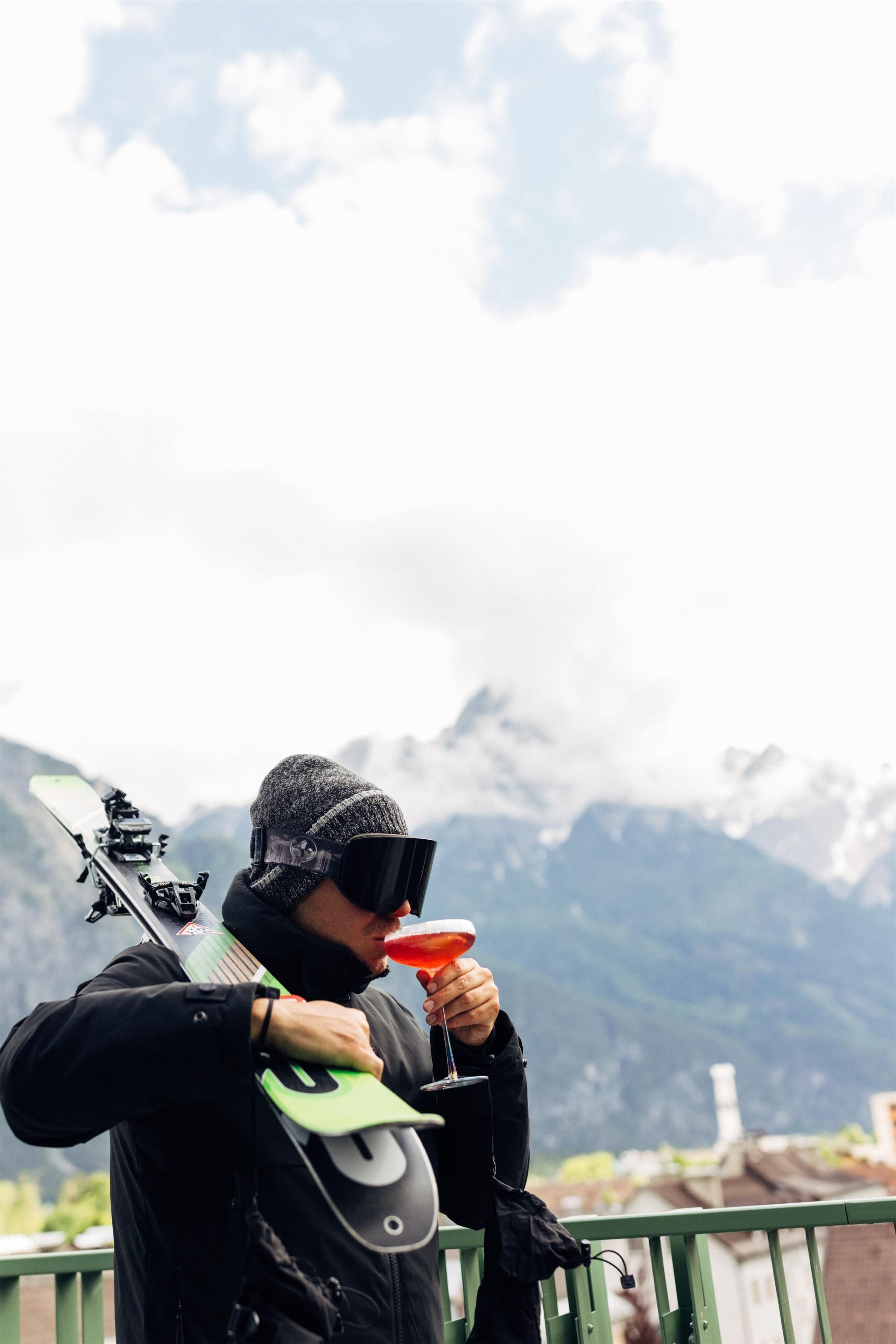 Una persona sosteniendo un arco y una flecha, de pie en un balcón con vistas a una montaña al fondo.