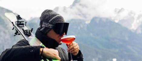 Una persona sosteniendo un arco y una flecha, de pie en un balcón con vistas a una montaña al fondo.