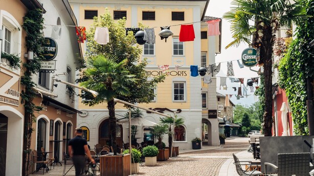 A cobblestone street with outdoor seating, a café, and a building with a sign reading "Gosse". - harry's home Lienz hotel & apartments (Lienz)
