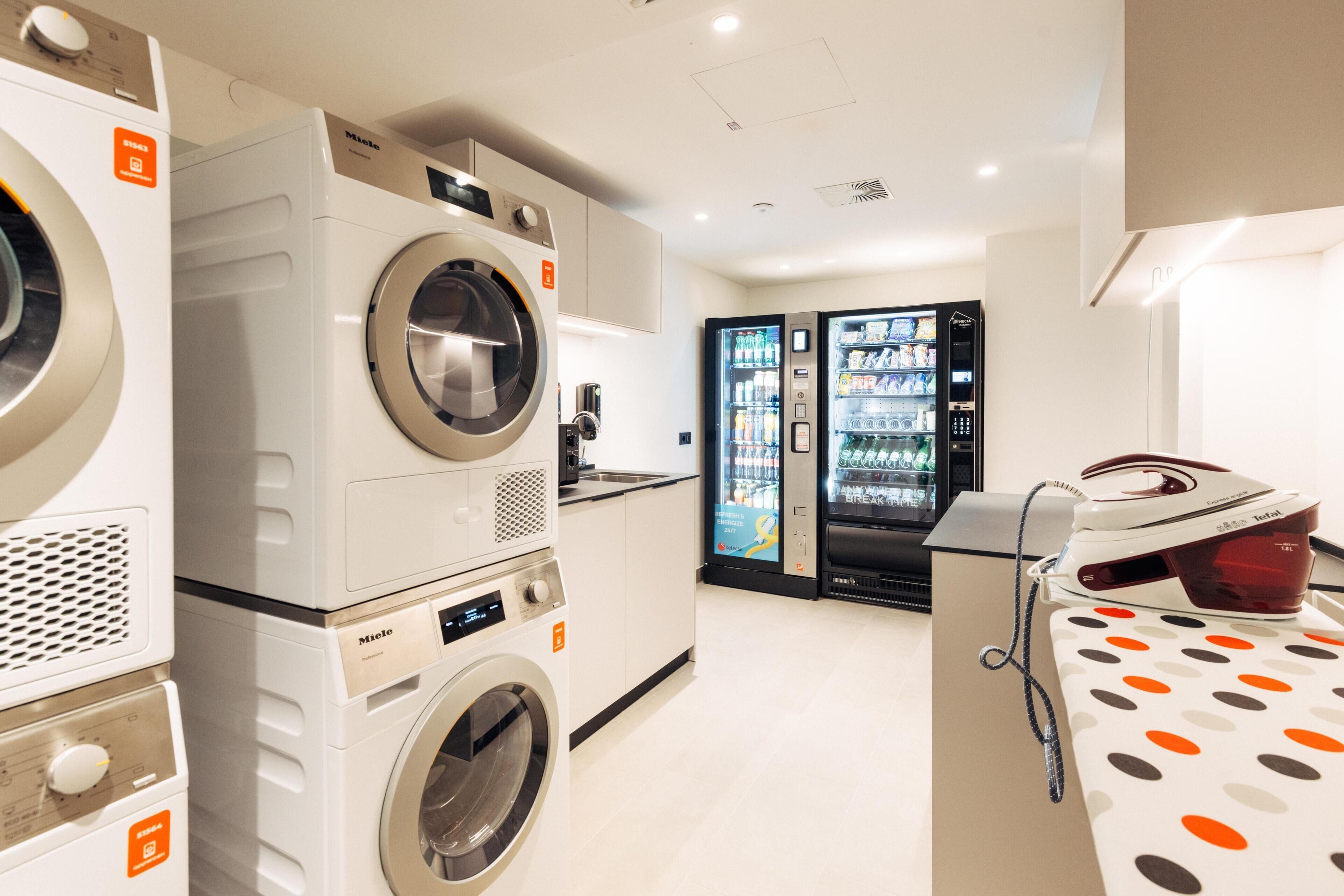 A laundry room with multiple washing machines, a refrigerator stocked with beverages, and a polka dot tablecloth.