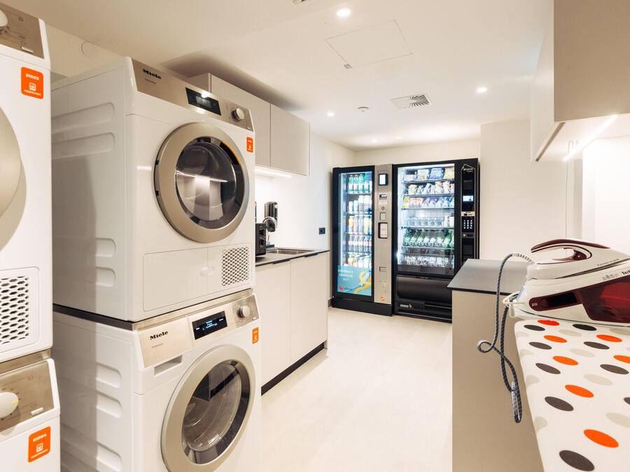 A laundry room with multiple washing machines, a refrigerator stocked with beverages, and a polka dot tablecloth.