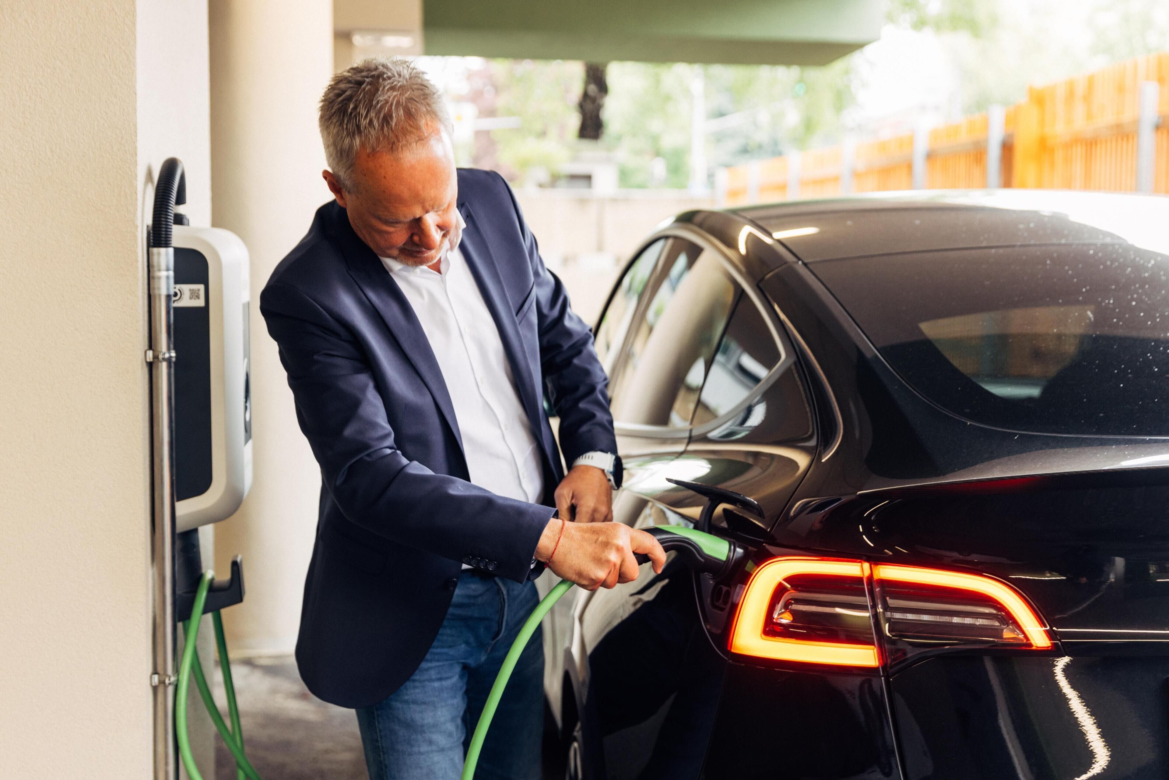 A man charging a black car at an electric vehicle charging station.