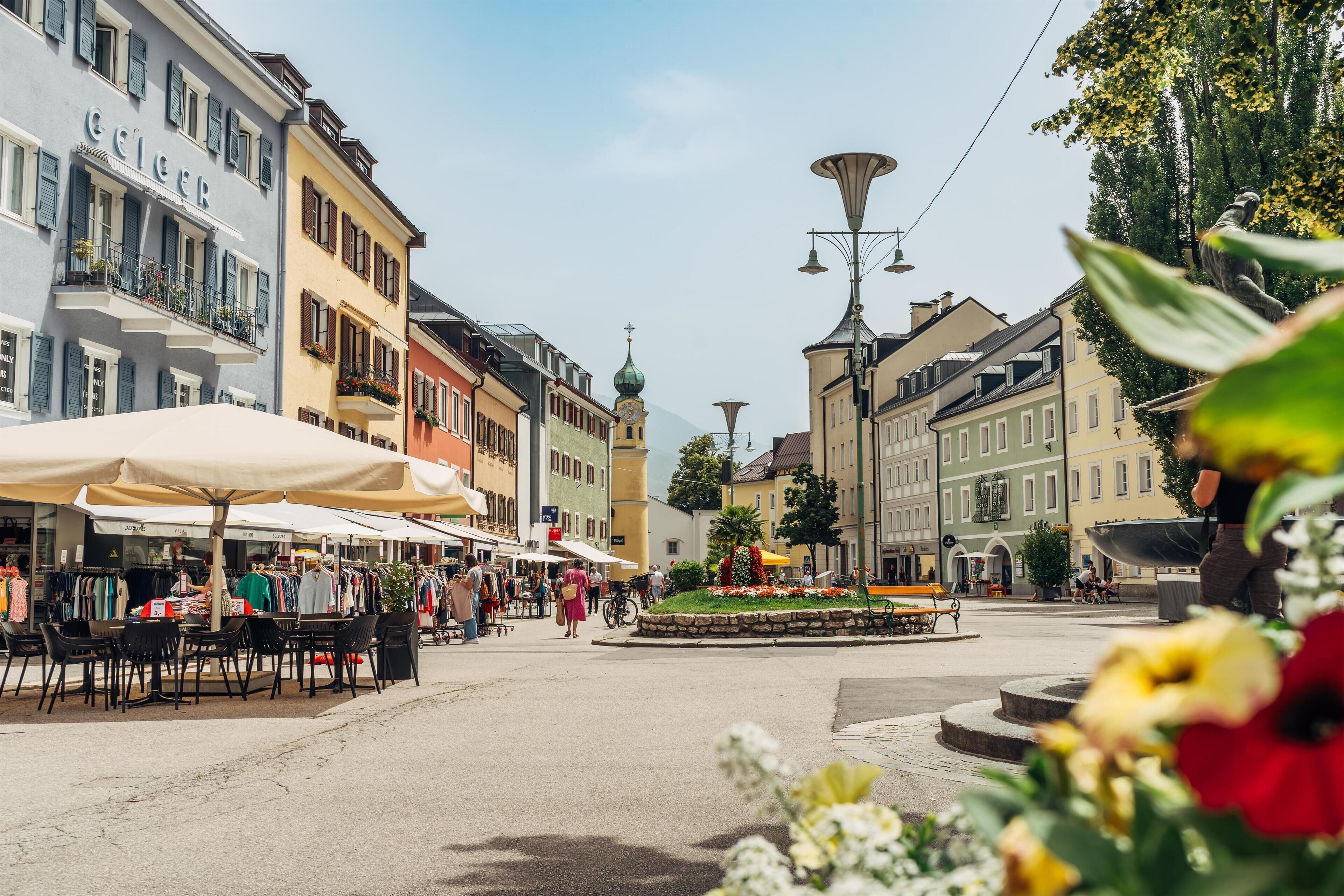 A bustling square with outdoor cafes, a central fountain, and historic buildings with balconies.