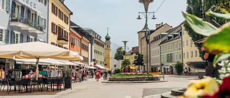 A bustling square with outdoor cafes, a central fountain, and historic buildings with balconies.