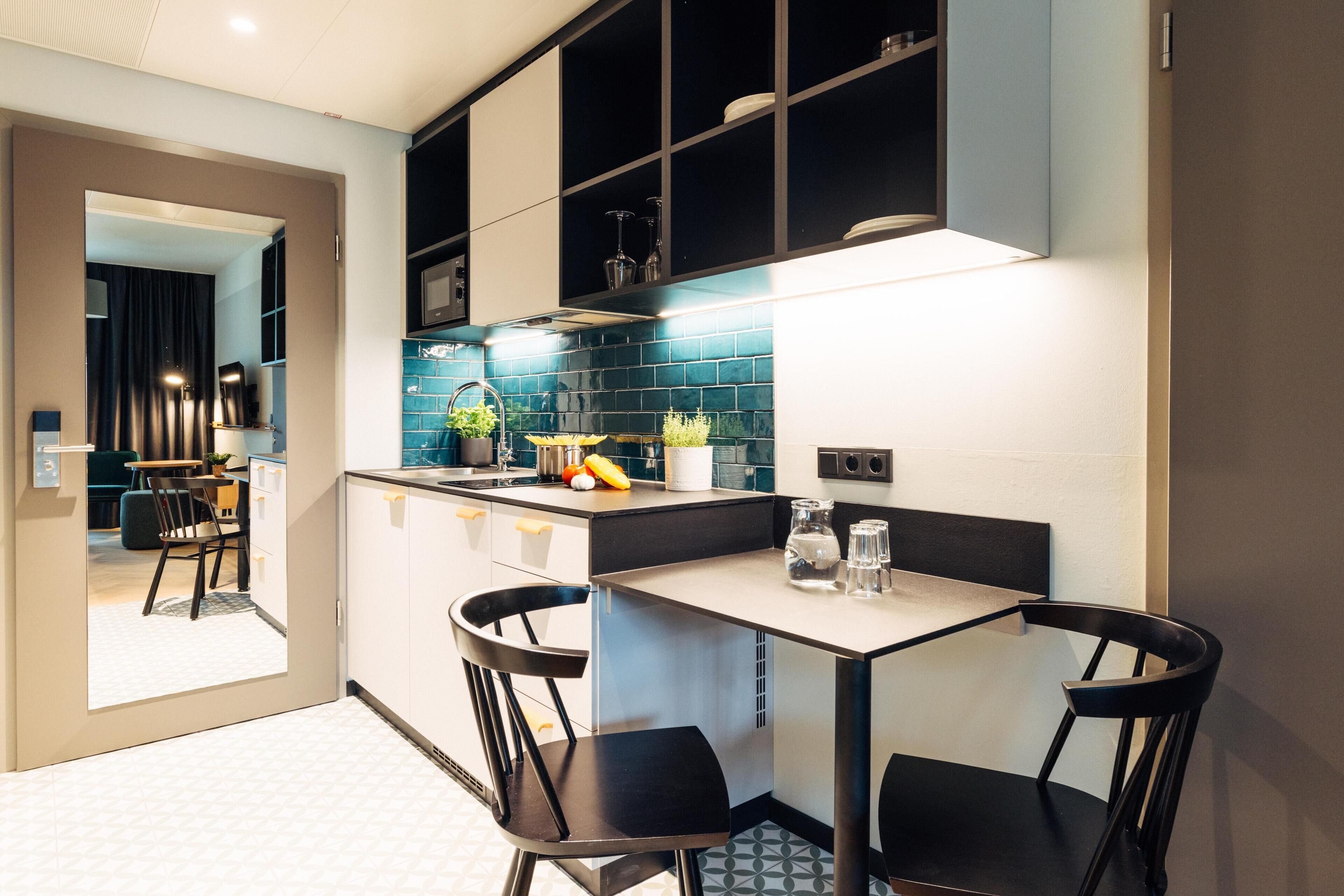 Cozinha moderna com área de jantar, incluindo uma ilha central, cadeiras pretas e painel de azulejos.