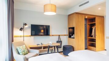 A modern hotel room with a bed, a desk, a chair, a TV, a wardrobe, and a hanging coat rack.